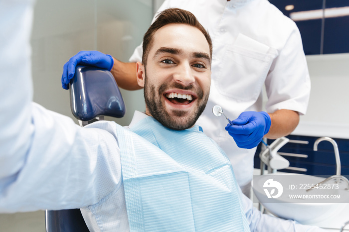 Handsome happy young man sitting in medical dentist center take a selfie by camera.