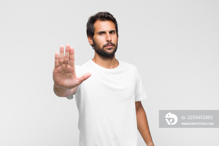 young latin handsome man looking serious, stern, displeased and angry showing open palm making stop gesture