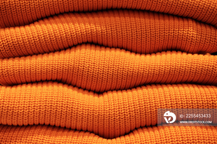 Pile of warm orange knitted sweaters in a row.