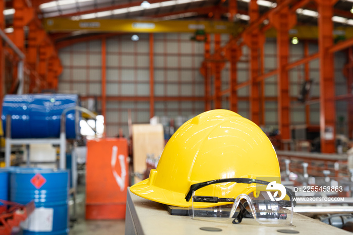 Selective focus at safety hardhat that put on the heavy machine inside of the factory production line. Safety and protection gear concept in industrial area to prevent injury of worker or accident.