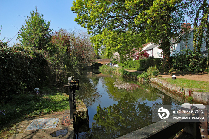 Basingstoke canal near Woking in Surrey on a sunny spring day with lock gates in the foreground and reflection of hump back bridge in the background