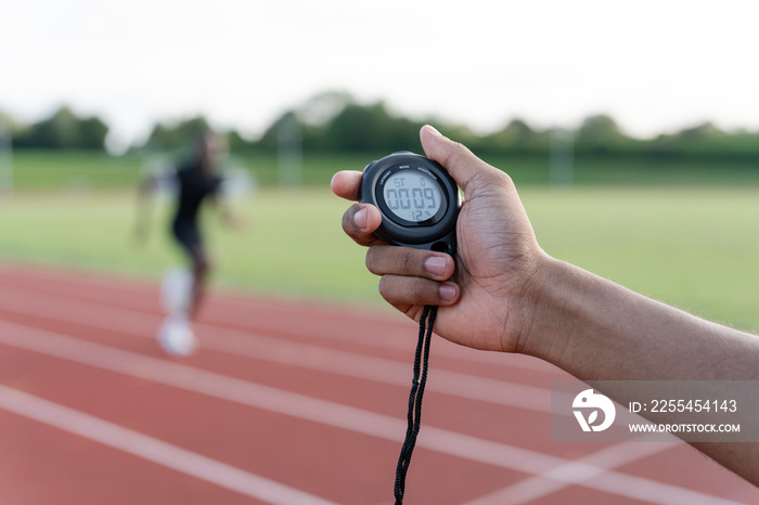 Male hand holding stopwatch during athletes sprint