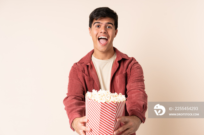 Handsome man over isolated background holding a big bucket of popcorns