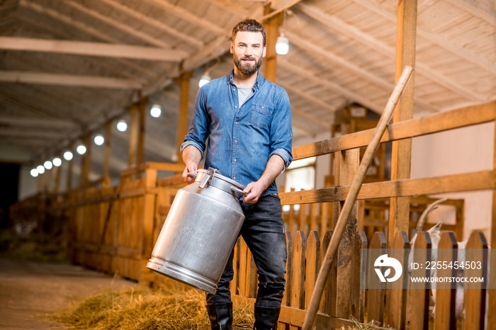 Portrait of a handsome farmer standing with retro milk container at the goat barn. Natural milk production and farming