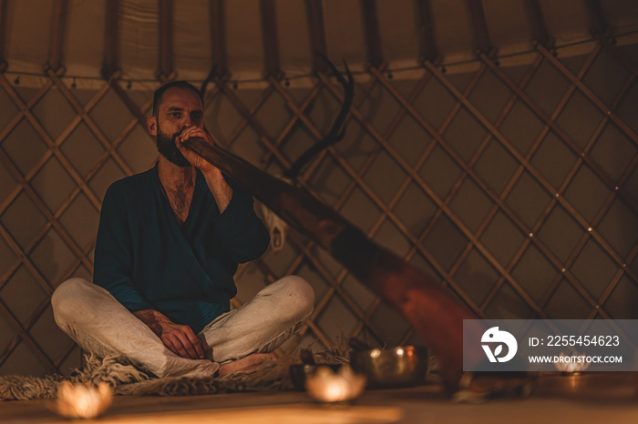 Man playng on didgeridoo by candlelight and tibetian bowl.