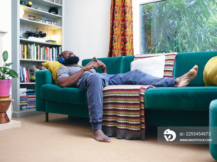 Man lying on sofa, listening to music on headphones