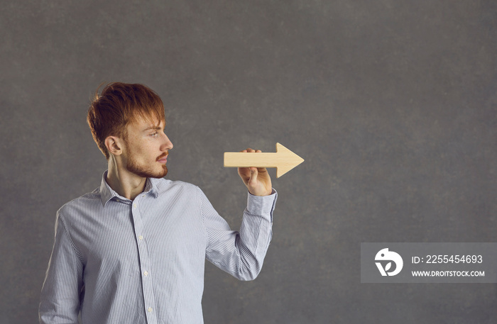 Studio headshot portrait of confident serious young businessman freelancer hold arrow with right direction. Millennial hipster guy in casual shirt showing business path way orientation