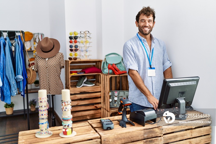 Young hispanic shopkeeper man smiling happy working at clothing store.