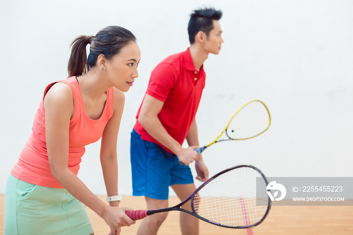 Side view of a beautiful and competitive Chinese woman holding the racquet while looking forward with concentration during a squash game with her partner