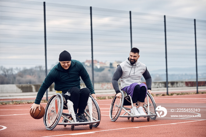 Happy men with disabilities playing wheelchair basketball on outdoor sports court.