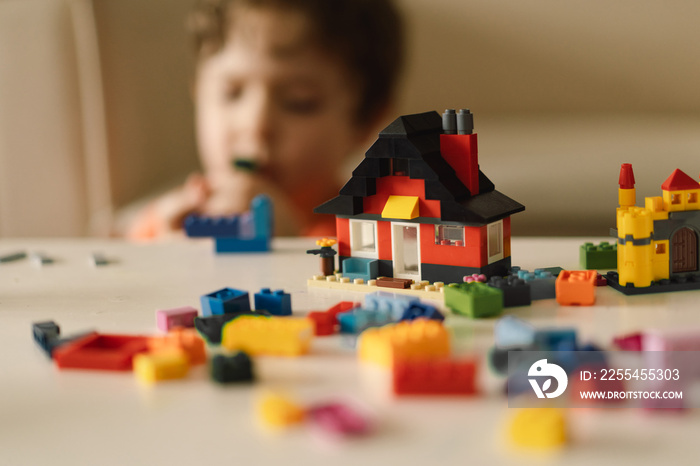 Cute boy is playing constructor at home. Kid playing block toys in home at nursery. Toddler having fun and building out of bright constructor bricks. Development and Construction Concept