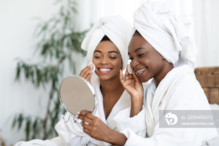 Attractive ladies applying face toner with pads, looking at mirror