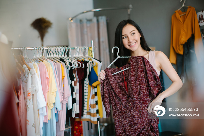 Positive woman choosing new clothes in shop and smiling