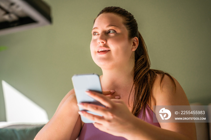 Positive girl with excess weight smiling with phone at her hands while chatting