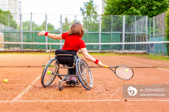 Disabled young woman on wheelchair playing tennis on tennis court.