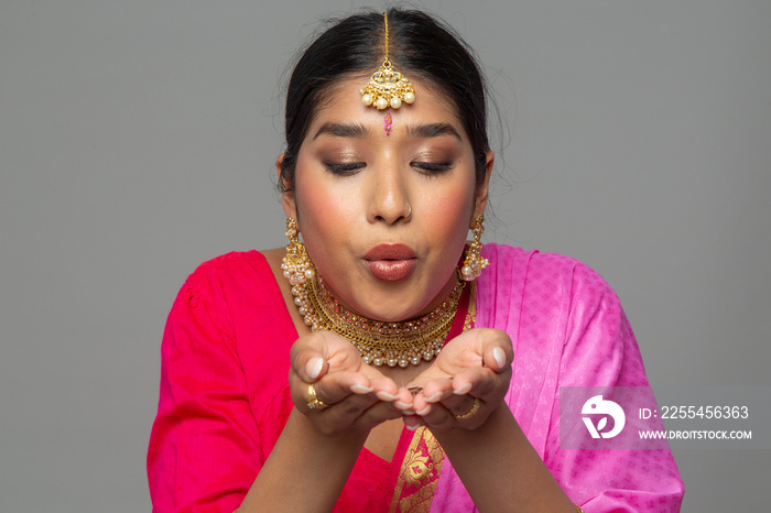 Studio portrait of woman wearing sari and gold jewelry blowing