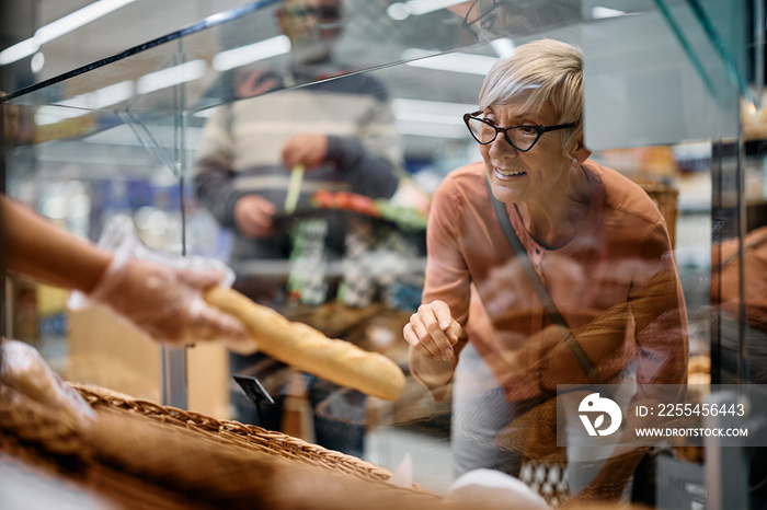 Happy senior woman choosing pastry at supermarket bakery.