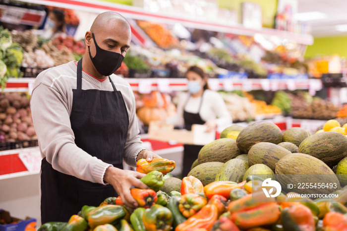 Supermarket employee in protective mask lays out bell peppers on the shelves