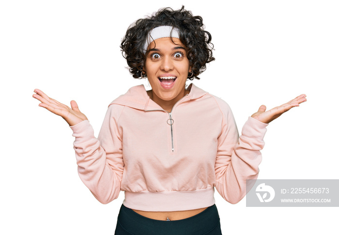 Young hispanic woman with curly hair wearing sportswear celebrating victory with happy smile and winner expression with raised hands