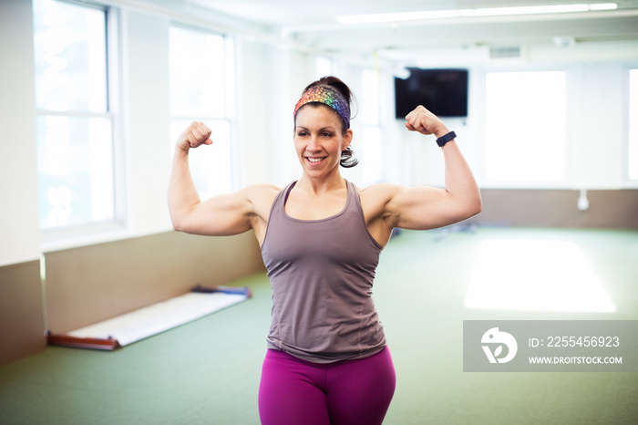 Smiling confident female athlete flexing muscles while standing in gym