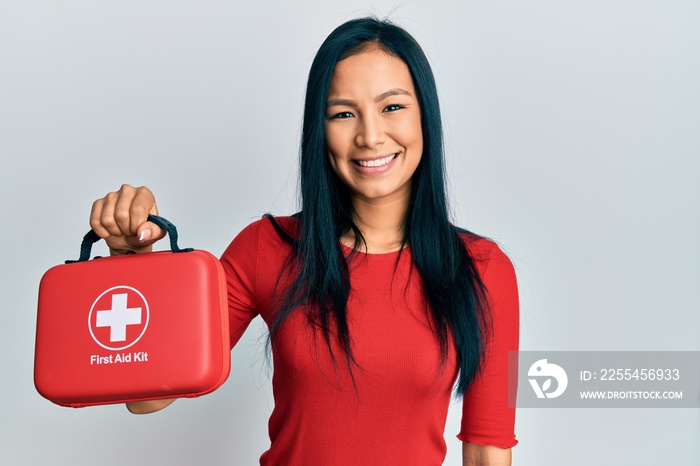 Beautiful hispanic woman holding first aid kit looking positive and happy standing and smiling with a confident smile showing teeth