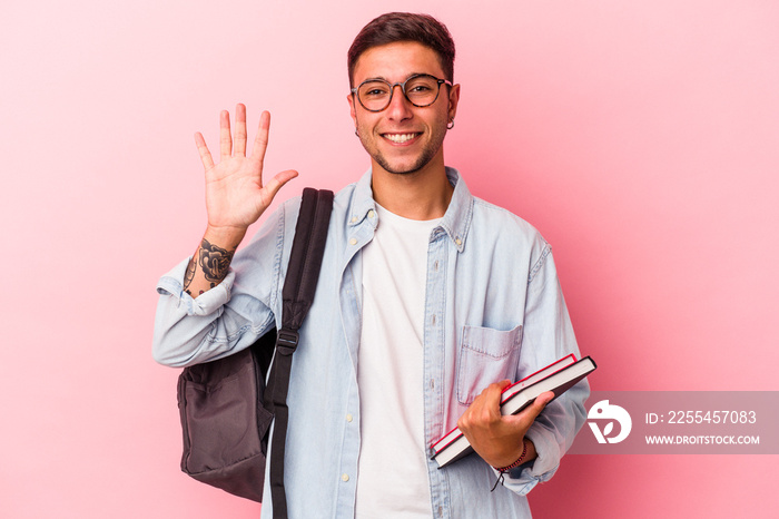 Young caucasian student man holding books isolated on pink background  smiling cheerful showing number five with fingers.