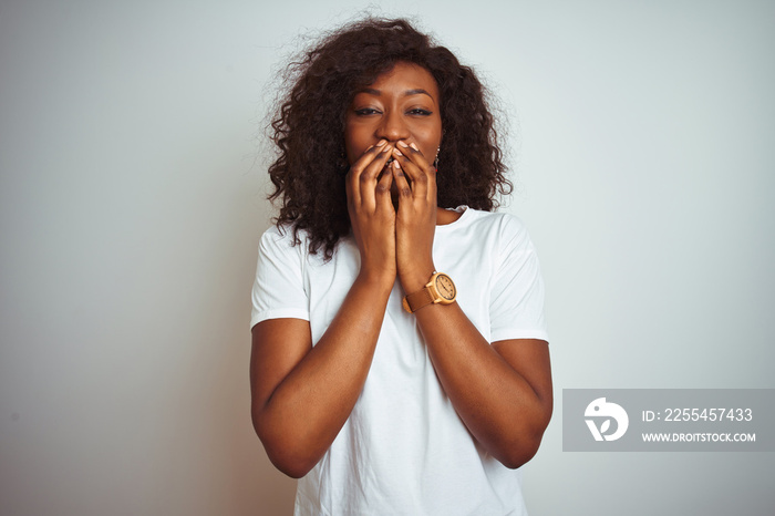 Young african american woman wearing t-shirt standing over isolated white background laughing and embarrassed giggle covering mouth with hands, gossip and scandal concept