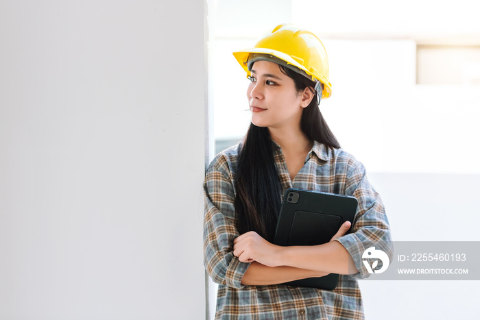 Portrait of asian woman construction worker holding digital tablet for work at building site, wearing hardhat and safety equipment for safe.