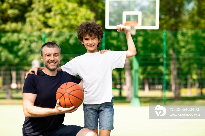 Man posing with strong boy on basketball pitch