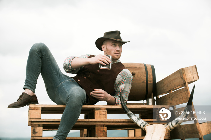 Cowboy on ranch. Handsome man in cowboy hat and retro vintage outfit. Attractive man with whiskey or brandy.