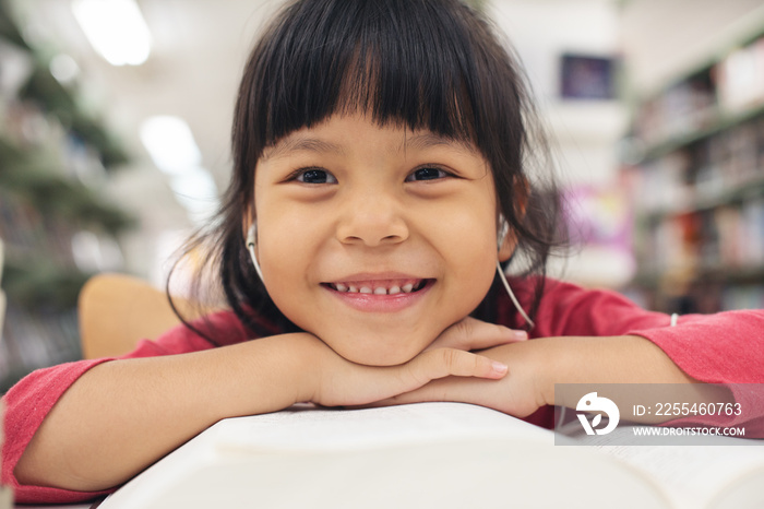 Portrait of a Smiling Little Asian Girl. Children smile and looking camera. happy asia kid in pink shirt and reading book  and listen music at library. Education people concept