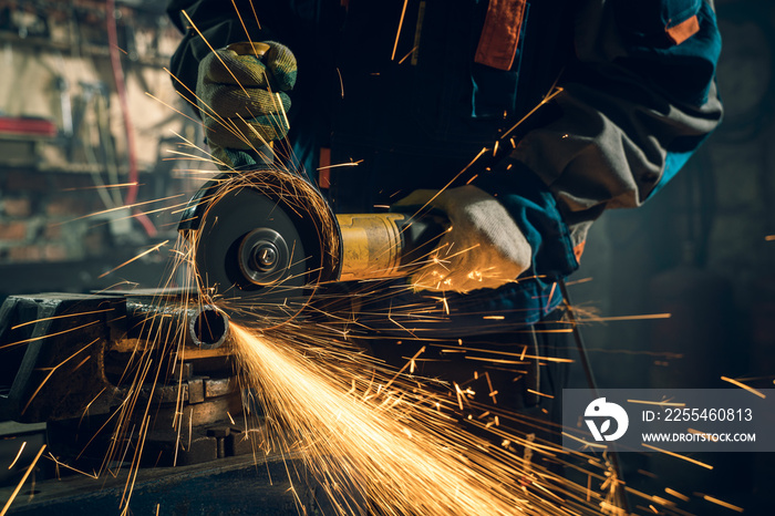 Locksmith in special clothes and goggles works in production. Metal processing with angle grinder. Sparks in metalworking