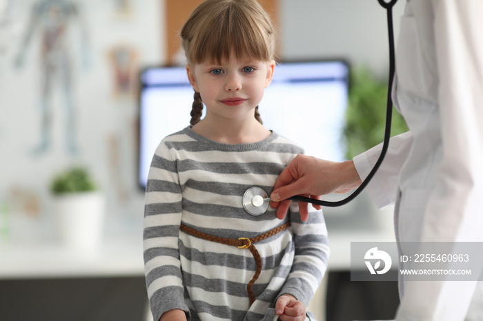 Pediatrician listens to heart with stethoscope to little girl in clinic’s office. Congenital heart disease diagnosis and treatment concept.