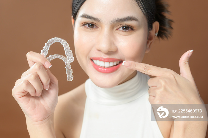 A young woman with beautiful teeth is holding Invisalign, healthy dental concept