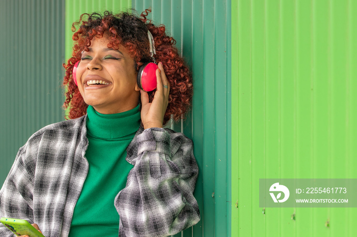 afro girl with headphones and phone outdoors on green wall background