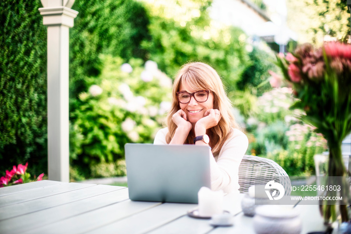 Happy mature woman having video call while sitting in the garden at home