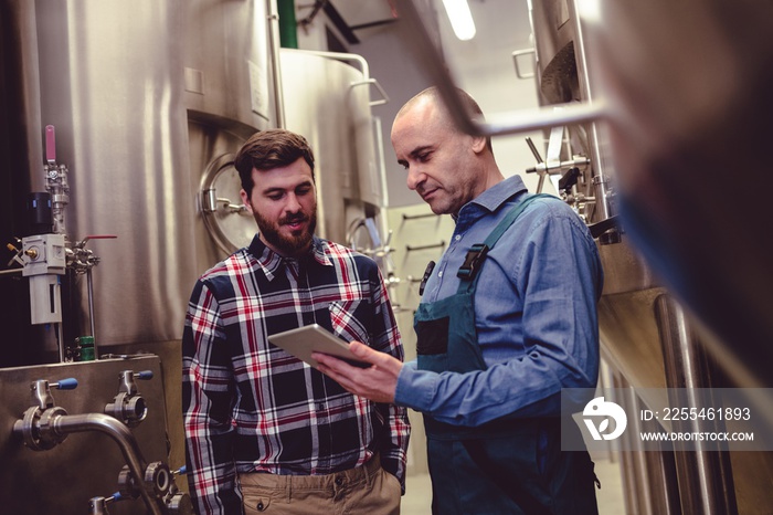 Worker and owner discussing over digital tablet at brewery