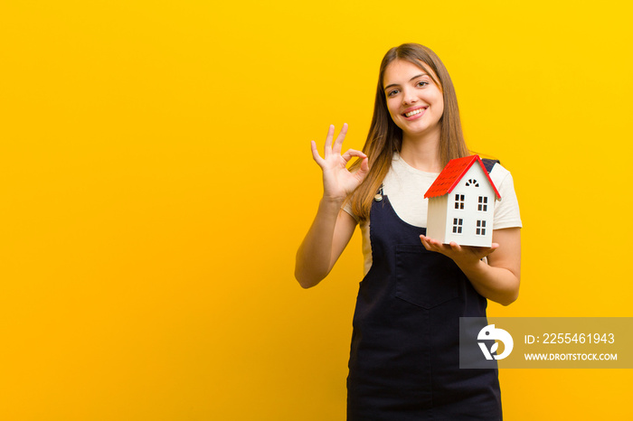 young pretty woman with a house model against orange background