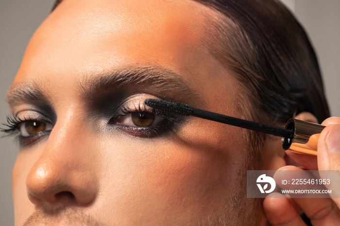 Makeup artist going to apply black mascara on eyelashes of male fashion model