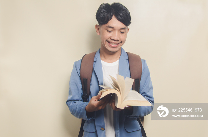 happy young asian man wearing college suit while carrying bag and books on isolated background