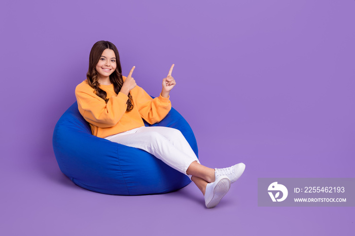 Full length photo of adorable cute lady wear sweatshirt bean bag pointing two fingers empty space isolated violet color background