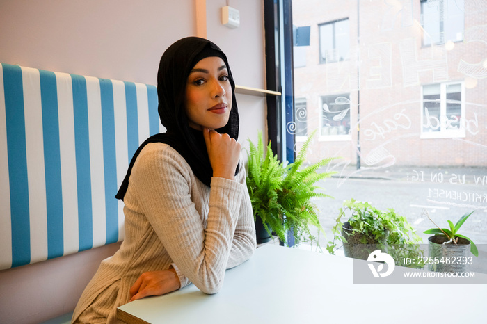 Portrait of young woman in hijab sitting in cafe