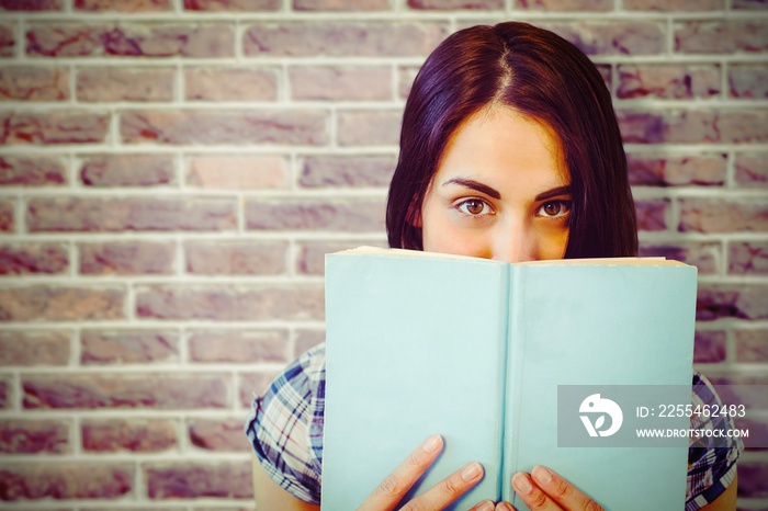 Composite image of close up portrait of woman hiding behind book