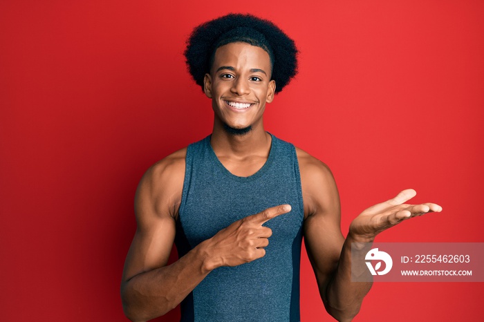 African american man with afro hair wearing sportswear amazed and smiling to the camera while presenting with hand and pointing with finger.