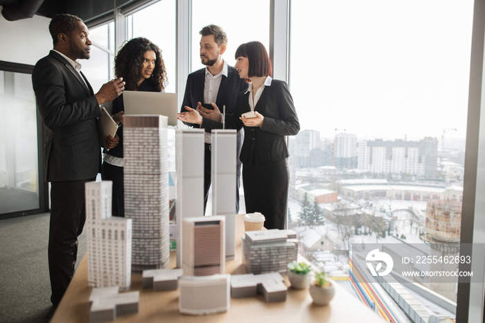 Business, company strategy, financial report concept. Team of diverse multiethnic businesspeople working with financial reports using laptop at open space office with white walls and panoramic windows