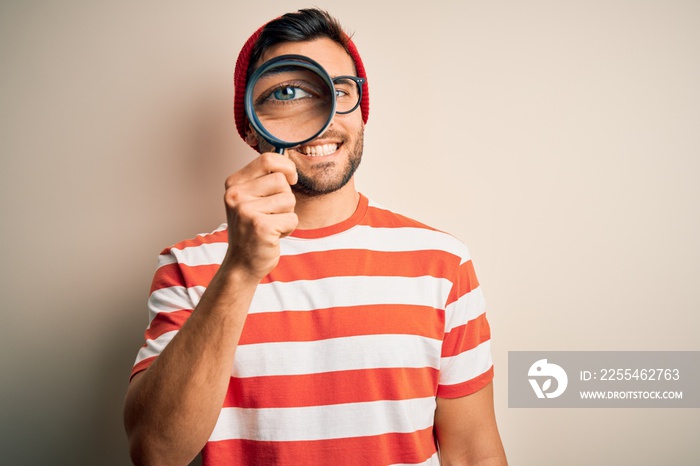 Young detective man looking through magnifying glass over isolated background with a happy face standing and smiling with a confident smile showing teeth