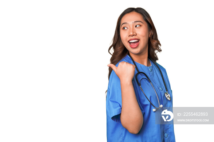 A young nurse chinese woman points with thumb finger away, laughing and carefree.