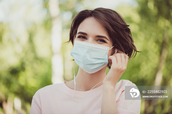 Photo of cute nice smiling young girl lady listen music earphones wear protective mask covid pandemic outbreak preventive means wear safety rules concept pink t-shirt park outdoors