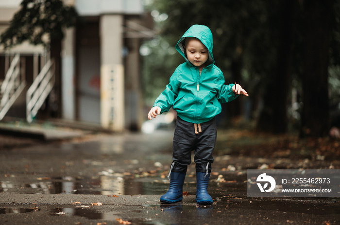 Happy boy playing outside on a rainy day wearing rubber boots and jacket