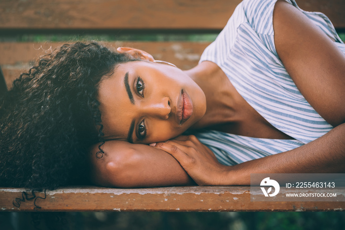 Beautiful young black woman laying down on a chair in a park